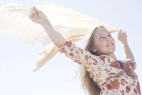 Chica sosteniendo un sarong flotante en el aire con los brazos extendidos contra un cielo azul . —  Fotos de Stock