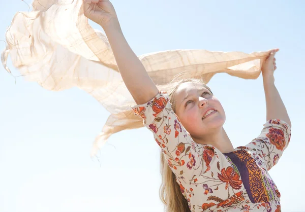 Young teenage girl holding a sarong in the air, blowing in the wind against a blue sky. — Stock Photo, Image