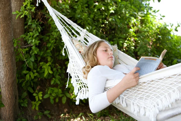 Junges Teenager-Mädchen liest ein Buch, während sie sich auf eine Hängematte im Garten legt. — Stockfoto