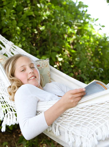 Porträt einer jungen Teenagerin, die ein Buch liest, während sie sich in einem Garten auf eine Hängematte legt. — Stockfoto