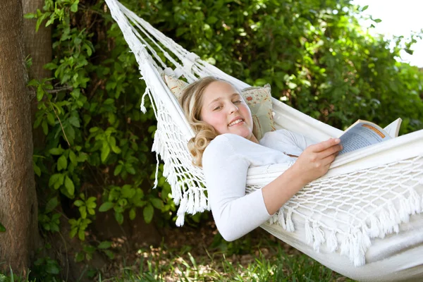 Porträt einer jungen Teenagerin, die ein Buch liest, während sie sich in einem Garten auf eine Hängematte legt — Stockfoto