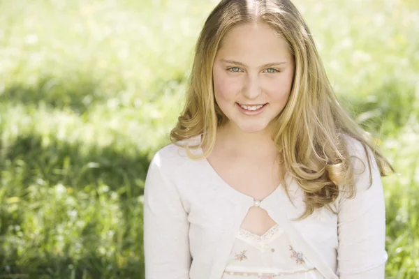 Retrato de uma menina em um campo de grama verde, sorrindo sob uma luz dourada . — Fotografia de Stock