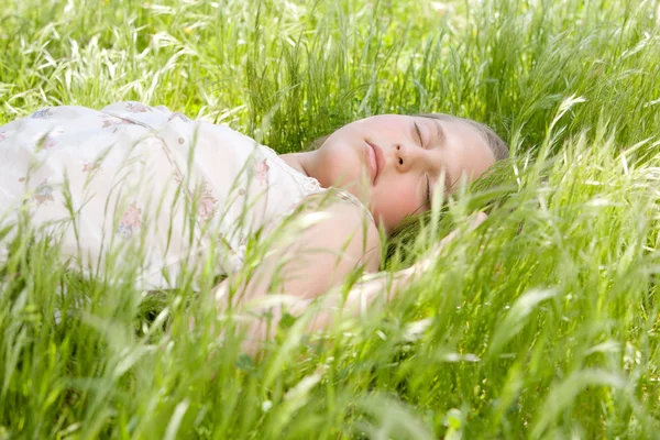 Närbild på en vacker ung blond flicka sover på långa gröna gräset i en trädgård. — Stockfoto