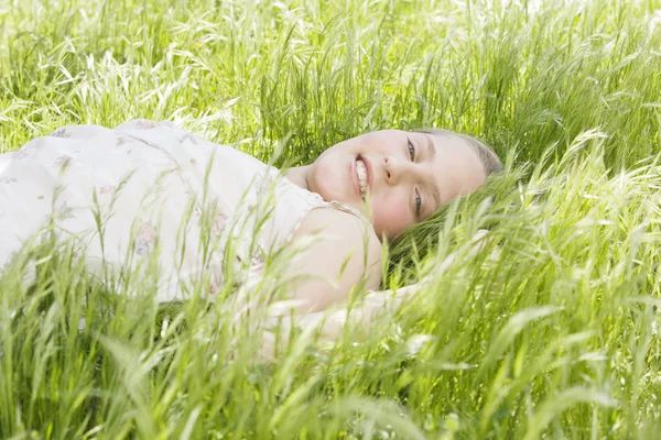 Retrato de niña acostada sobre hierba verde larga en un jardín, sonriendo . — Foto de Stock