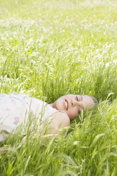 Porträt eines Mädchens, das sich lächelnd auf ein langes grünes Gras legt. — Stockfoto