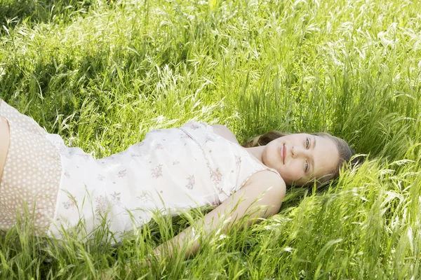 Retrato de menina que estabelece em grama verde longa no jardim . — Fotografia de Stock