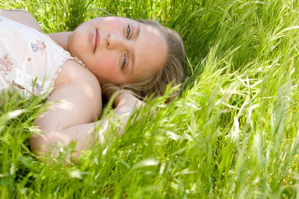 Jovem adolescente deitado em um longo jardim de grama verde, olhando para a câmera . — Fotografia de Stock