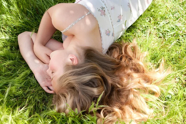 Junges Teenagermädchen schläft, während sie sich im Sommer im Garten auf langes grünes Gras legt. — Stockfoto