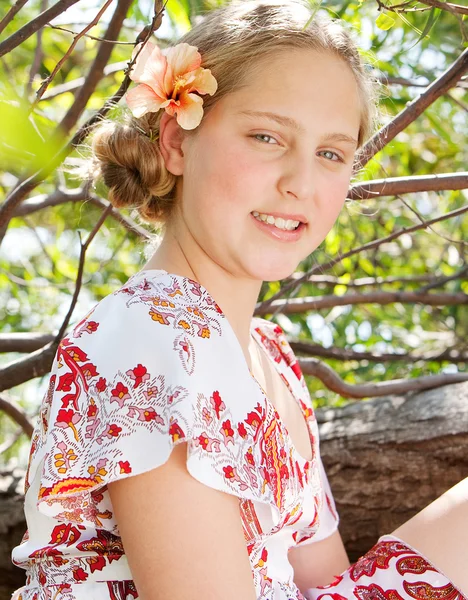 Schönes junges Mädchen sitzt auf einem Baumstamm und trägt eine Blume im Haar — Stockfoto
