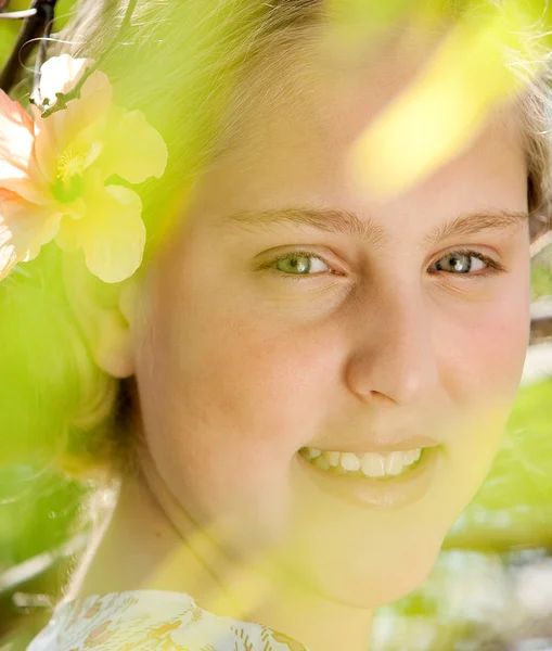 Portret van een mooie jonge blonde meisje met groene bladeren op de voorgrond close-up. — Stockfoto