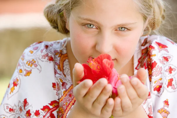 Retrato de cerca de una adolescente oliendo flores de hibisco, sonriendo . — Foto de Stock