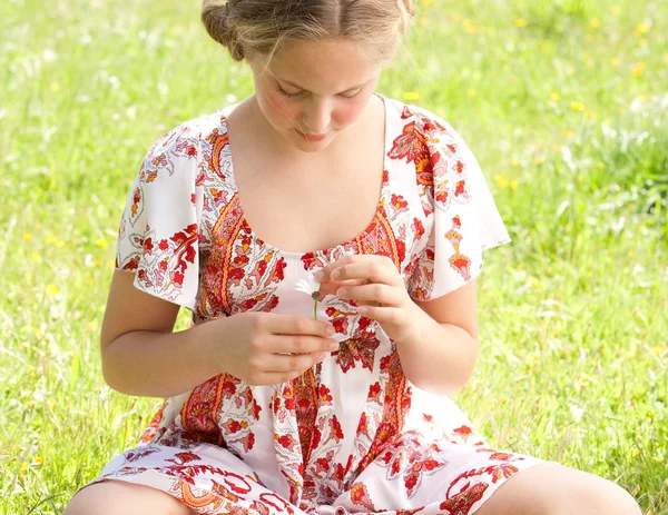 Jonge tiener trekken bloemblaadjes van een bloem daisy, spelen op liefde me love me niet. — Stockfoto