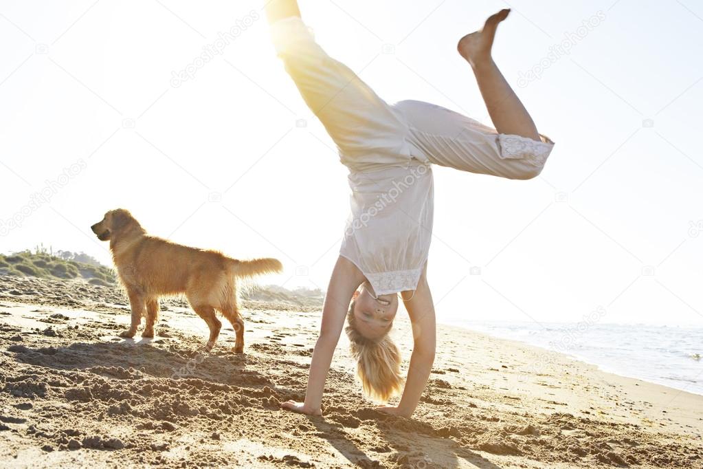 Girl with dog on the beach, doing carthweels with the sun filtering through.