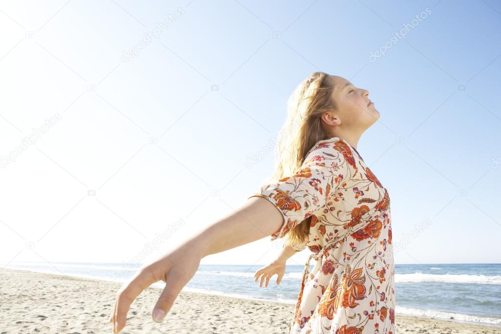 Girl breathing fresh air while standing by the shore on a white sand beach.