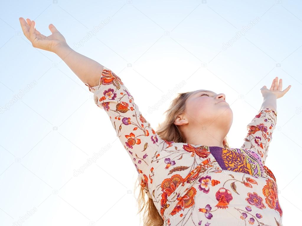 Young girl breathing fresh air with her arms raised against a blue sky.