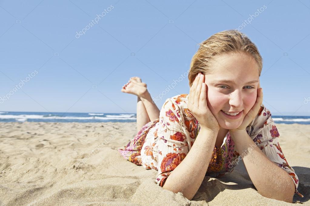 Girl laying down on a golden sand beach, smiling at the camera and