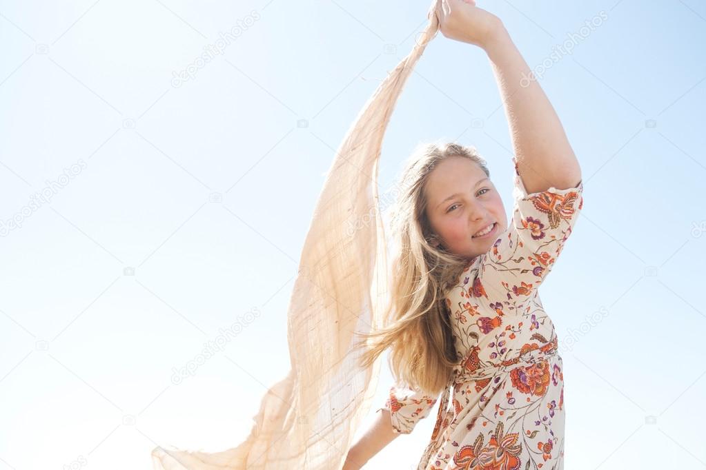 Young teenager holding a sarong in the air, blowing in the wind against a blue sky.