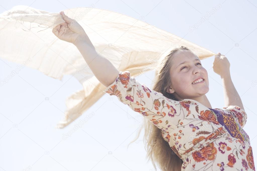 Girl holding a floating sarong in the air with arms outstretched against a blue sky.
