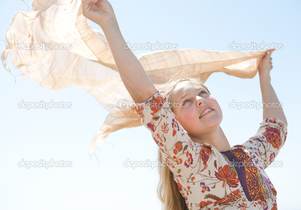 young teenage girl holding a sarong in the air, blowing in the wind against a blue sky.