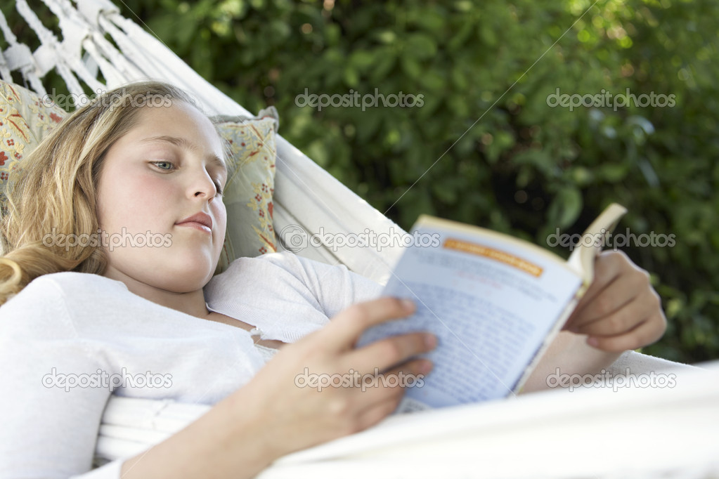 Portrait of girl reading a book while laying down on a hammock in the garden.
