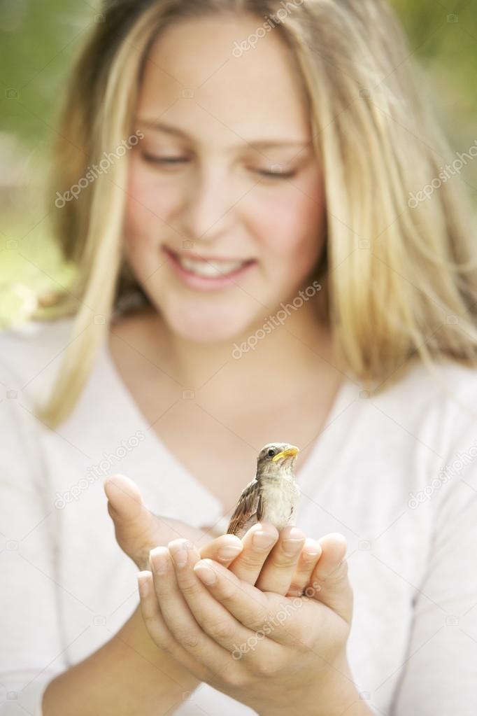 girl in the garden, holding a bird in her hands and smiling.