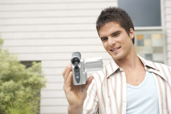 Young man using a digital video camera in home garden. — Stock Photo, Image