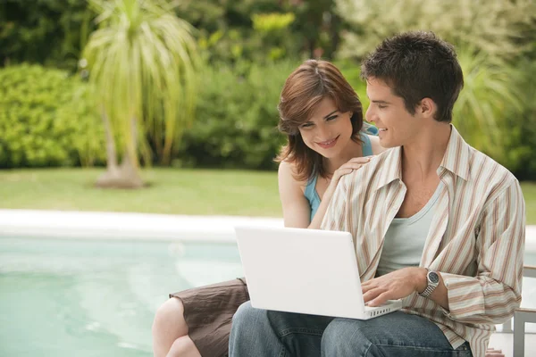 Paar met behulp van een laptop door zwembad, hotel buitenkant. — Stockfoto