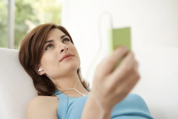 Jonge vrouw luisteren naar muziek met een mp3-speler, een bank thuis opleggen. — Stockfoto