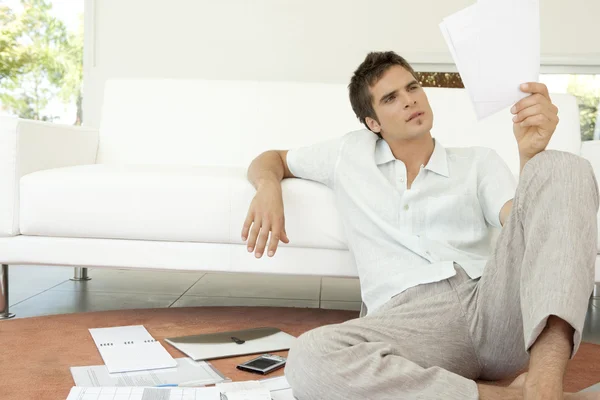 Junger Mann arbeitet an seinen Finanzen, sitzt auf dem Fußboden neben dem Sofa. — Stockfoto