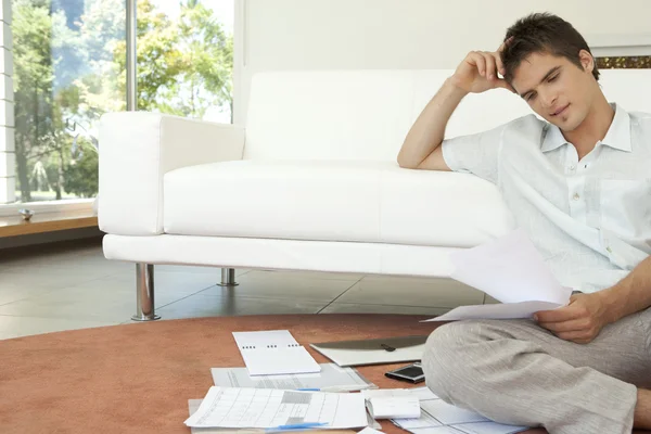 Junger Mann arbeitet an seinen Finanzen, sitzt auf dem Fußboden neben dem Sofa. — Stockfoto