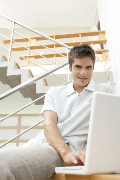 Jeune professionnel utilisant un ordinateur portable assis dans une cage d'escalier moderne . — Photo