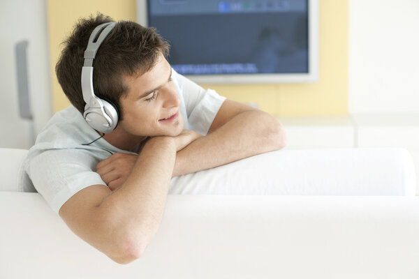 Молодой человек слушает музыку в наушниках дома
.