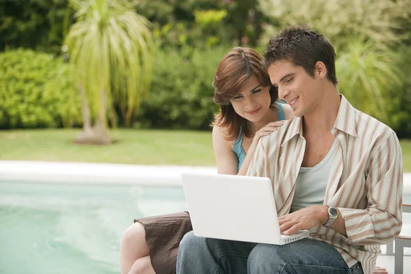 Paar mit einem Laptop zu Hause am Pool, Außenbereich. Stockbild