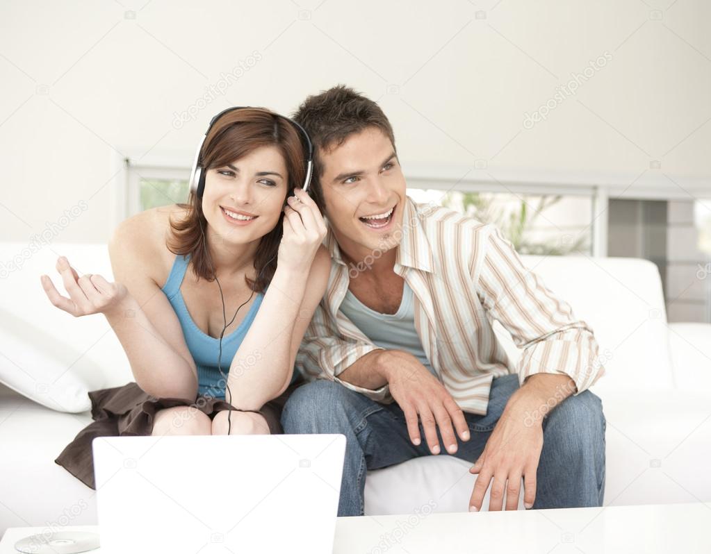 Man and woman using a laptop and listening to headphones at home.