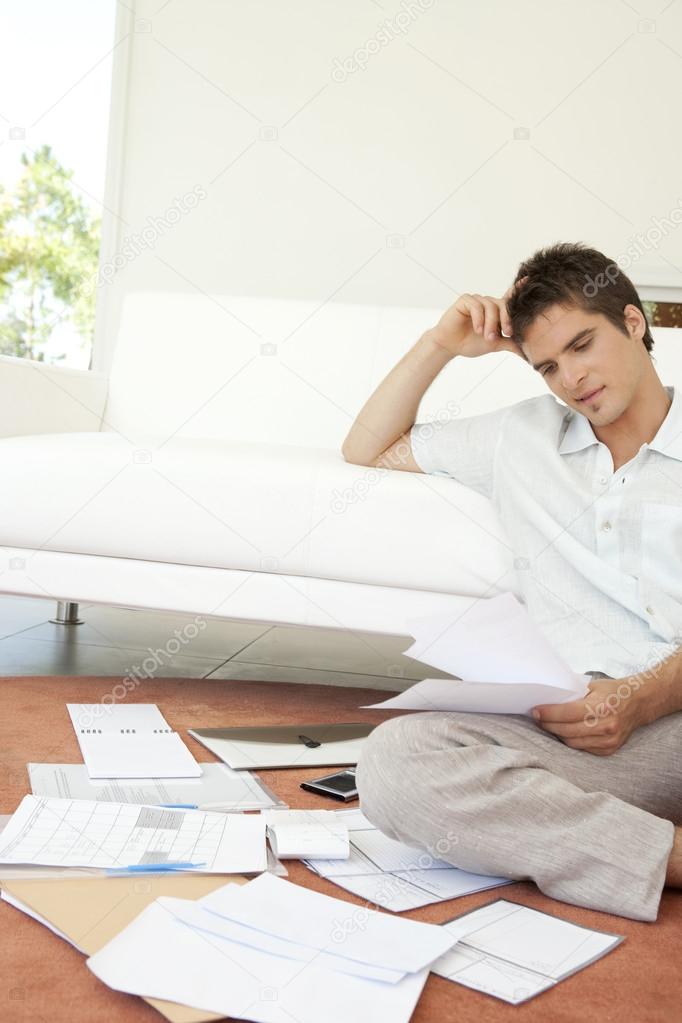 Young man working on his finances, sitting on the floor by the sofa.