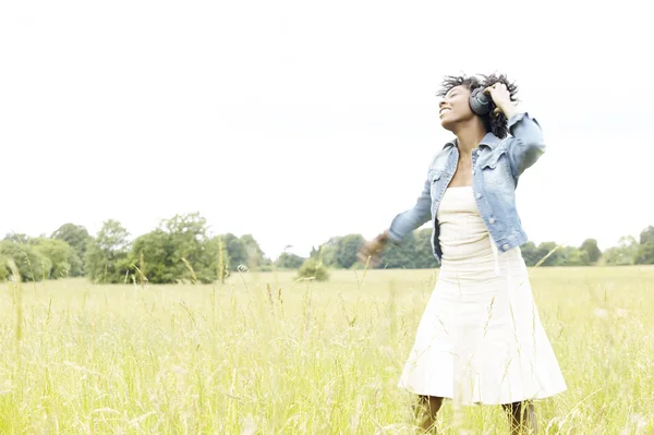 Ung kvinna dans i ett långt gräs medan du lyssnar på hennes hörlurar. — Stockfoto