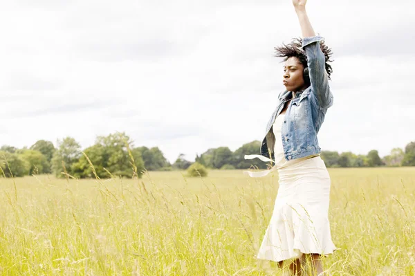 Joven mujer negra bailando en un campo de hierba mientras escucha música —  Fotos de Stock