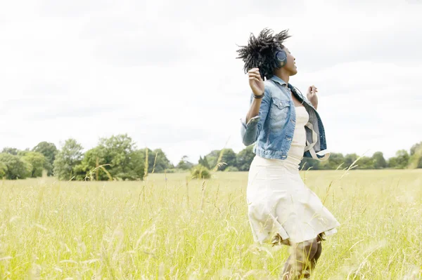 Joven mujer negra bailando en un campo de hierba mientras escucha música —  Fotos de Stock