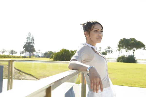 Ung kvinna lutande på en metallisk ledstång i en park — Stockfoto