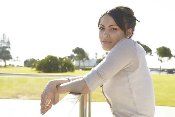 Young woman leaning on a metallic banister in a park — Stock Photo, Image