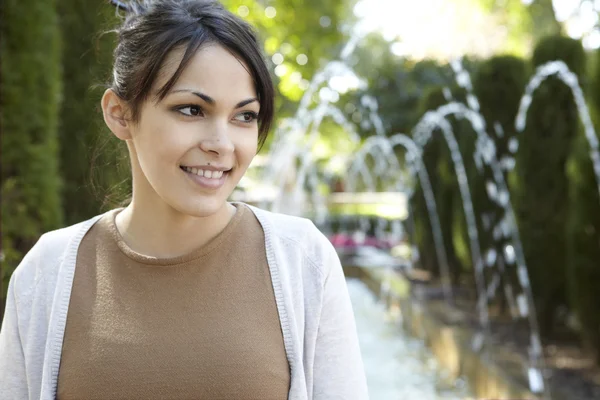 Giovane donna in piedi in un parco accanto a una fontana — Foto Stock