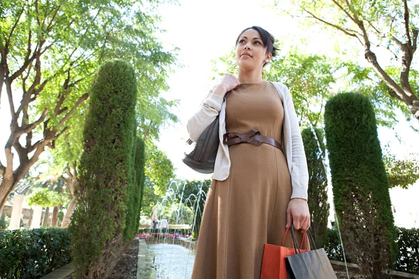 Atractiva joven mujer sosteniendo sus bolsas de compras mientras está de pie cerca de una fuente —  Fotos de Stock