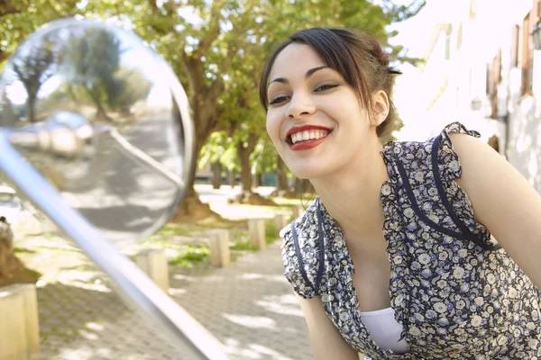 Young woman with red lips looking at herself in a motorbike's mirror — Stock Photo, Image