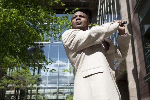 Businessman swinging a golf club in the middle of the city. — Stock Photo, Image