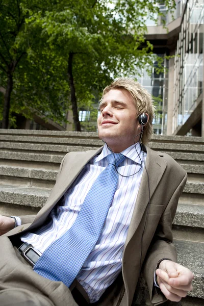 Young businessman listening to music with headphones while sitting down on some steps in the city. — Stock Photo, Image