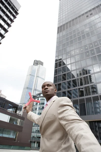 Businessman throwing a boomerang while standing in the middle of the financial district. — Stock Photo, Image