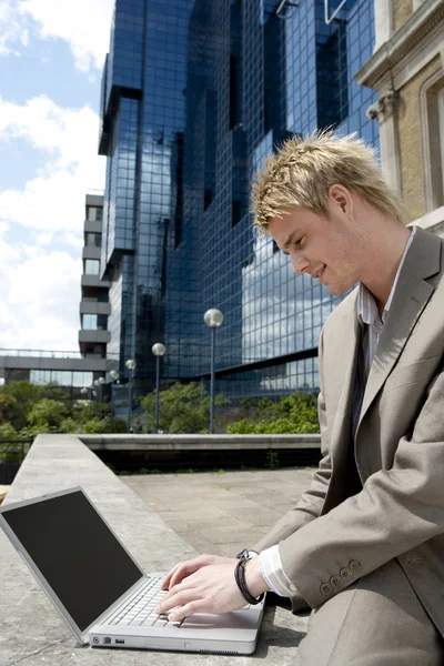 Young businessman typing on a laptop computer while sitting by modern office building — Stok fotoğraf