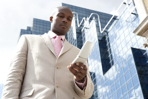 Homme d'affaires utilisant un téléphone portable, debout près d'un immeuble de bureaux réfléchissant . — Photo