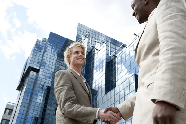 Deux hommes d'affaires serrant la main devant un immeuble moderne en verre de la ville . — Photo