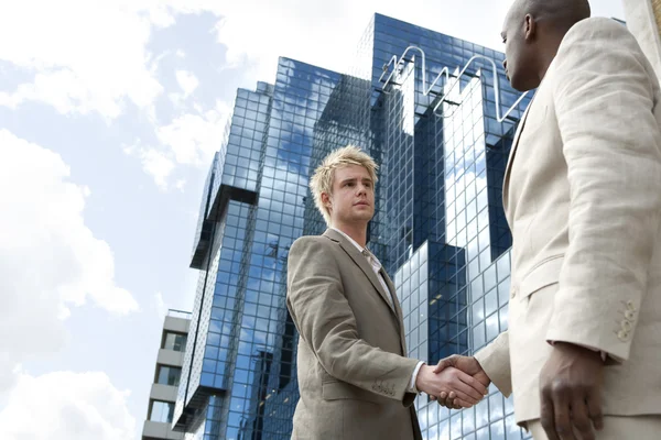 Twee zakenlieden schudden handen voor een glas modern gebouw in de stad. — Stockfoto